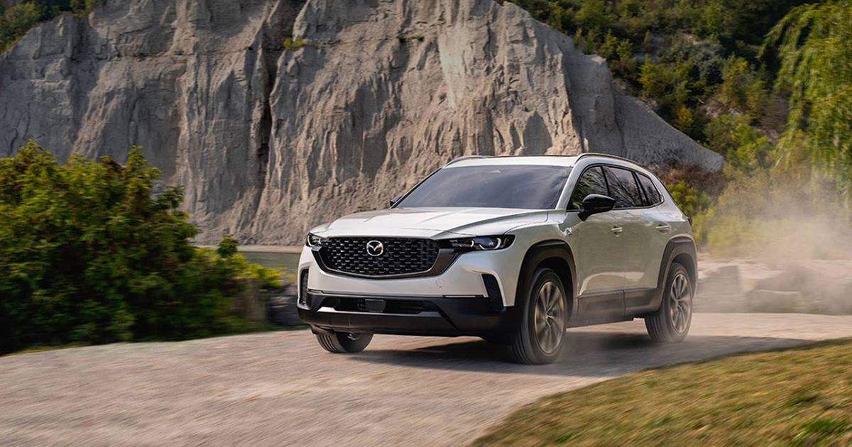 White SUV kicking up dust while driving near rocky cliffs.