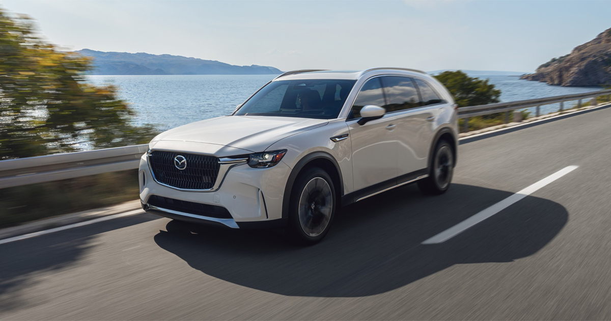 White SUV driving along a coastal highway with the ocean in the background.