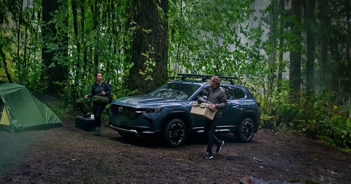 Mazda CX-50 SUV at forest campsite with tent and camping gear