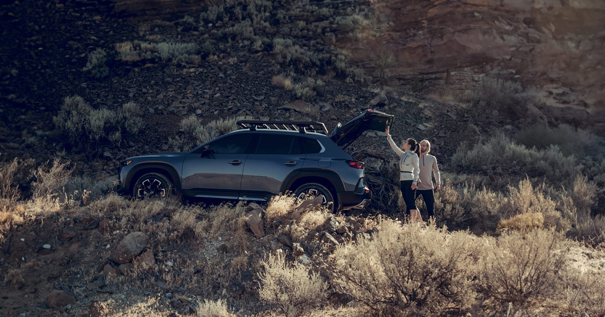 Mazda CX-50 SUV parked on rocky hillside with couple loading gear
