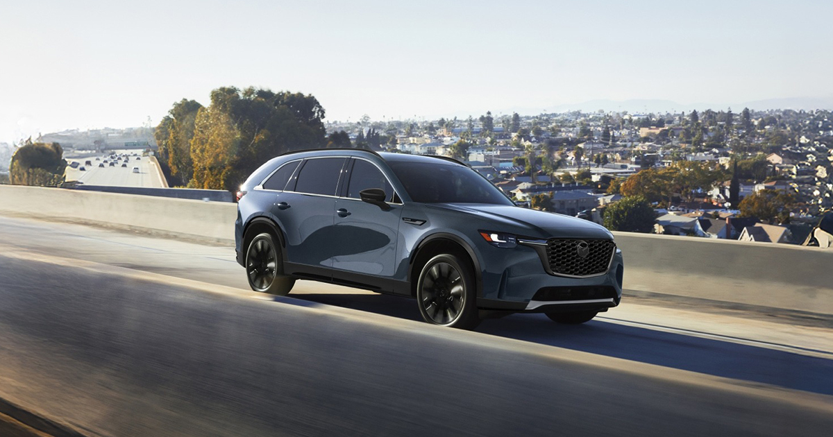 Blue Mazda CX-90 driving on highway with city in background