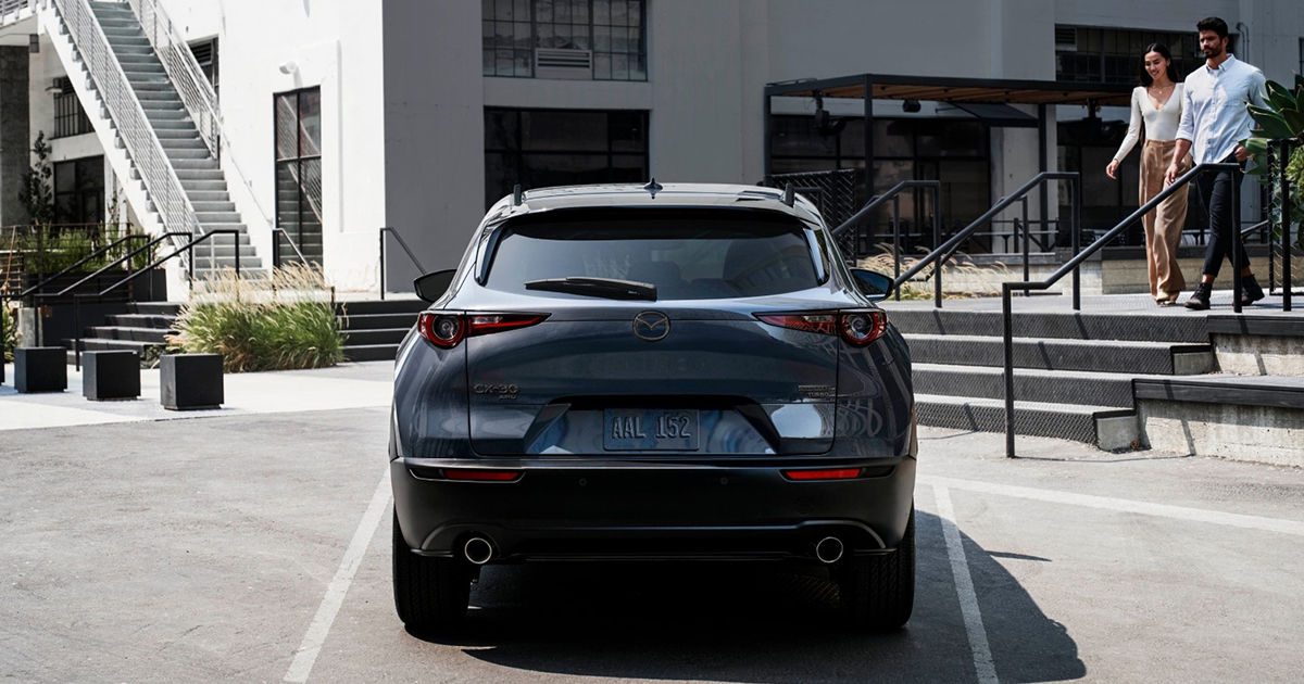 Rear view of Mazda CX-30 parked in urban setting with couple approaching