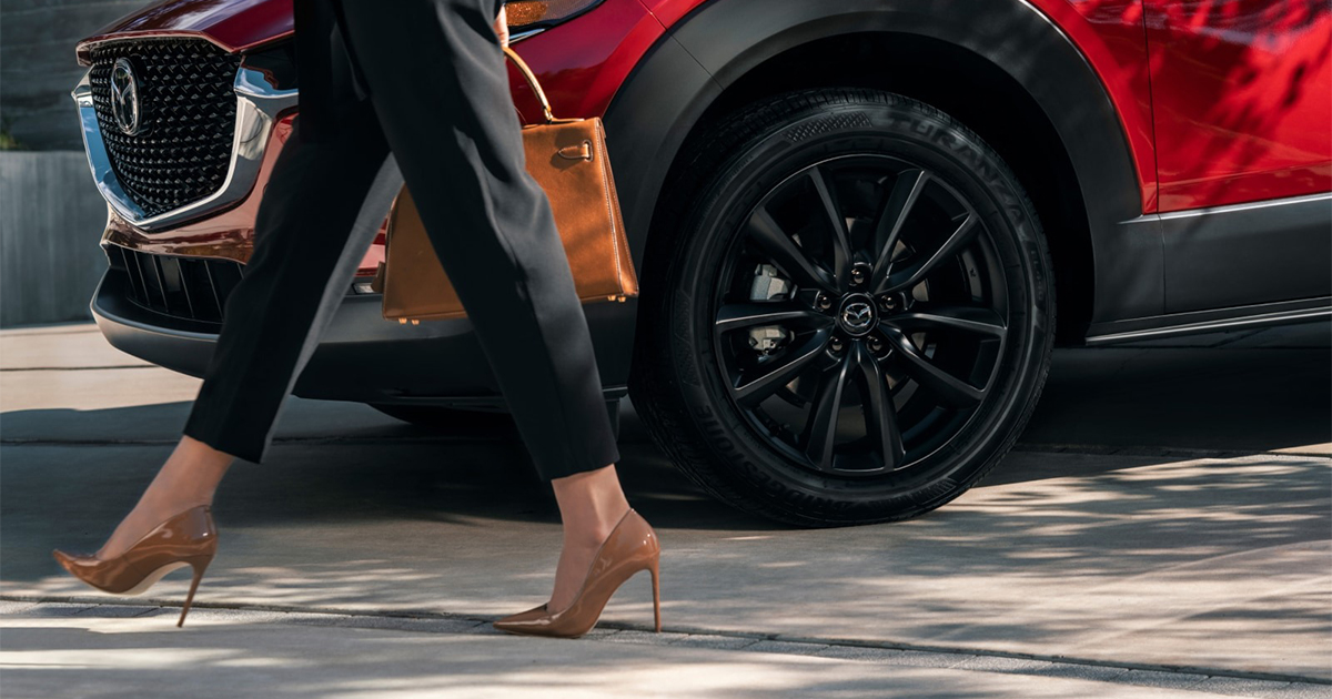 Close-up of red Mazda CX-30 black alloy wheel with woman walking past