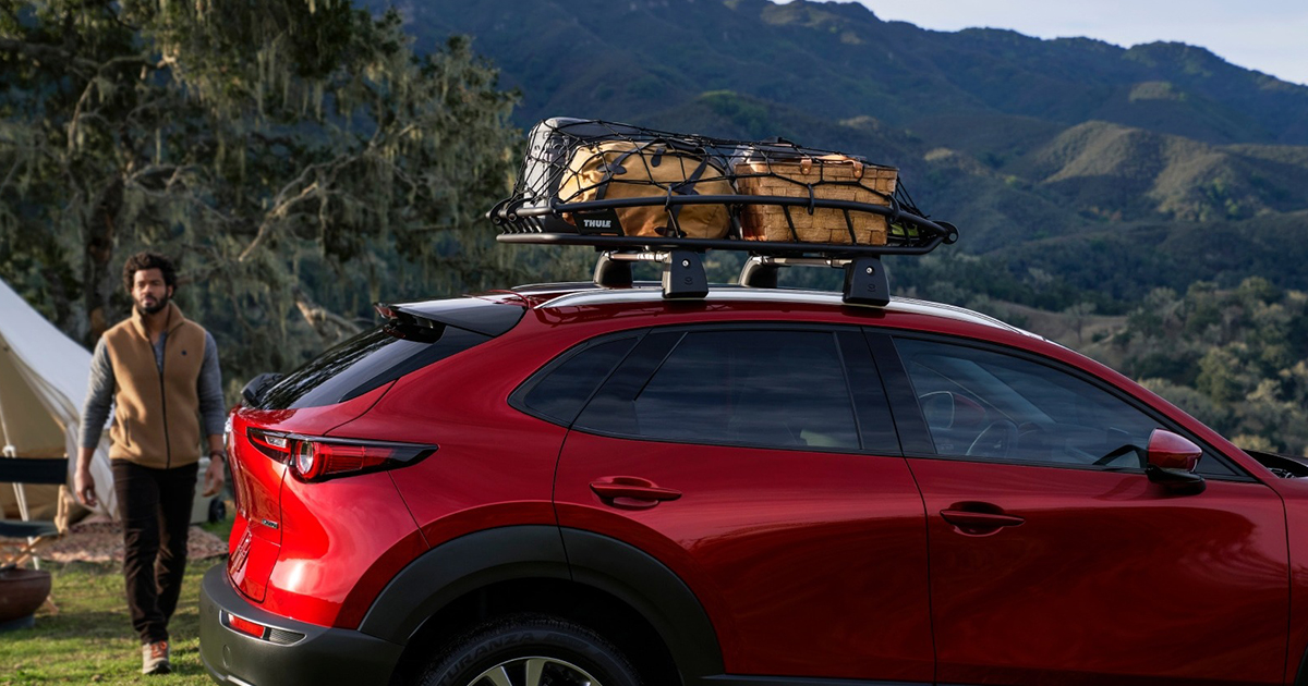 Red Mazda CX-5 SUV with roof rack carrying camping gear outdoors