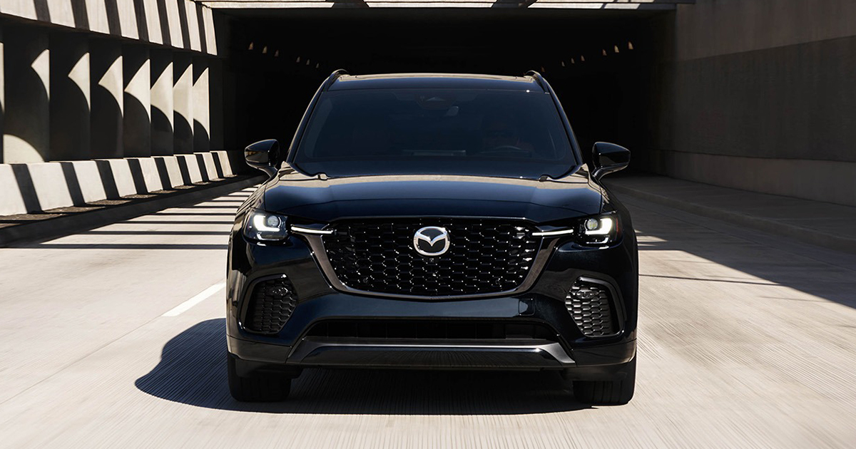 Front view of a black Mazda CX-90 SUV driving out of a tunnel with headlights on.