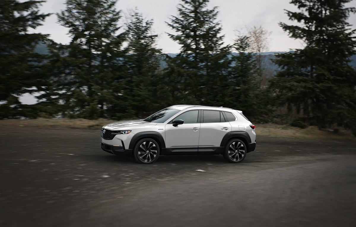 White 2026 Mazda CX-50 driving with forest in the background